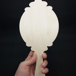 May include: A wooden hand mirror with a decorative, ornate frame and a long handle. The mirror is blank and ready to be painted or decorated.