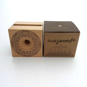 May include: A wooden speaker with a mandala design on the front. The speaker is made of natural wood and has a small hole in the center for sound to come out. The speaker is packaged in a brown cardboard box with the words "ecosound&reg;" and "natural speaker" printed on it.