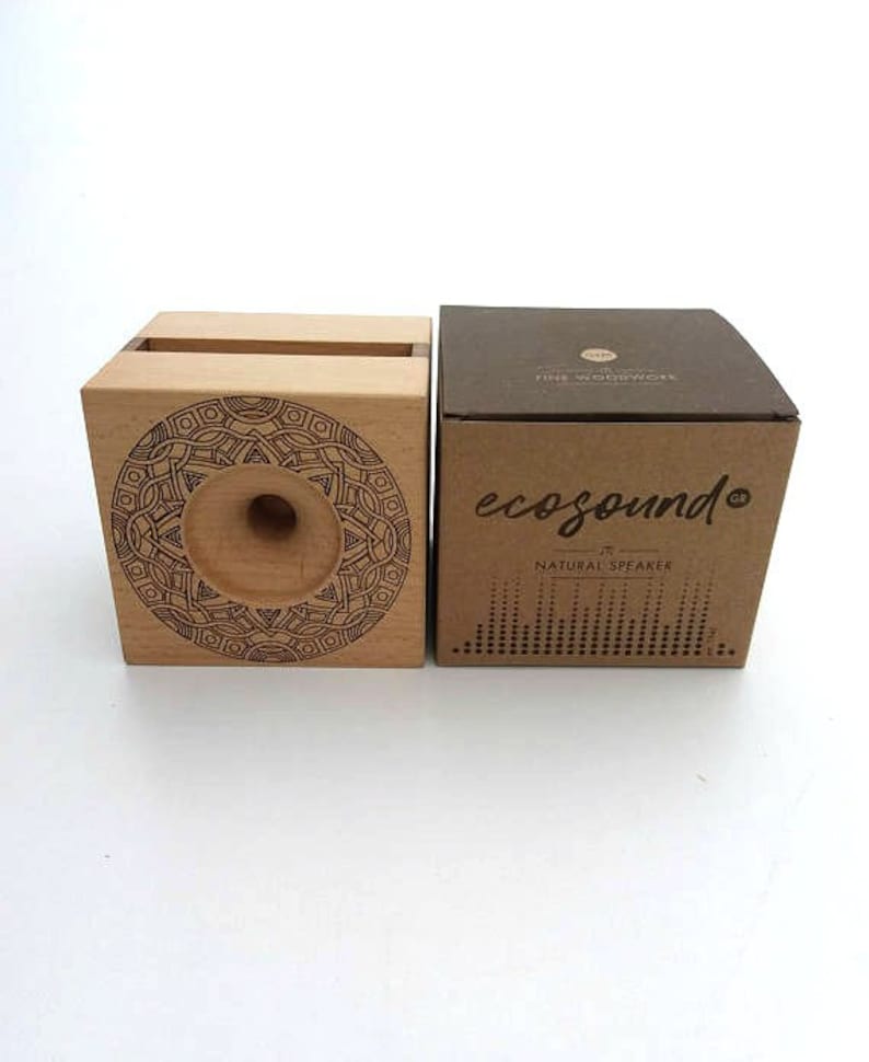 May include: A wooden speaker with a mandala design on the front. The speaker is made of natural wood and has a small hole in the center for sound to come out. The speaker is packaged in a brown cardboard box with the words "ecosound&reg;" and "natural speaker" printed on it.