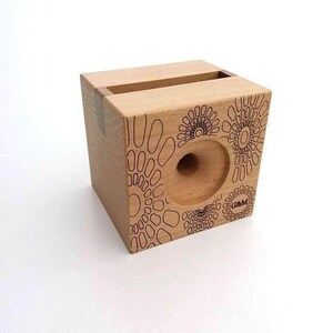 May include: A wooden phone stand with a geometric pattern and the text "G&M" on the side. The stand has a slot for holding a phone.