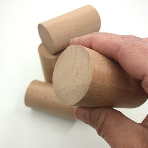 K&ouml;nnte beinhalten: Ein Satz aus vier Holzzylindern, von denen einer von einer Hand gehalten wird. Die Zylinder sind alle gleich gro&szlig; und gleich geformt und aus hellem Holz gefertigt.