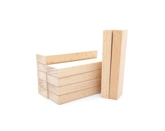 May include: A stack of light-colored wooden blocks, with a few blocks standing upright. The blocks are rectangular and appear to be unfinished. The image is set against a white background.