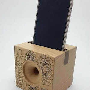 May include: A wooden phone stand with a circular cutout for sound amplification. The stand has a geometric pattern and the text "G&M" engraved on the front.