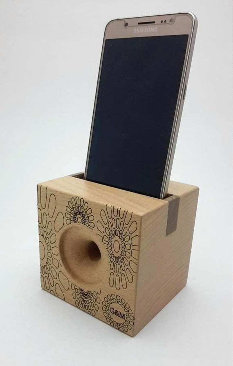 May include: A wooden phone stand with a circular cutout for sound amplification. The stand has a geometric pattern and the text "G&M" engraved on the front.