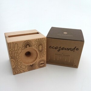 May include: A wooden speaker with a circular cutout and a geometric pattern. The speaker is packaged in a brown box with the text "ecosound" and "natural speaker".