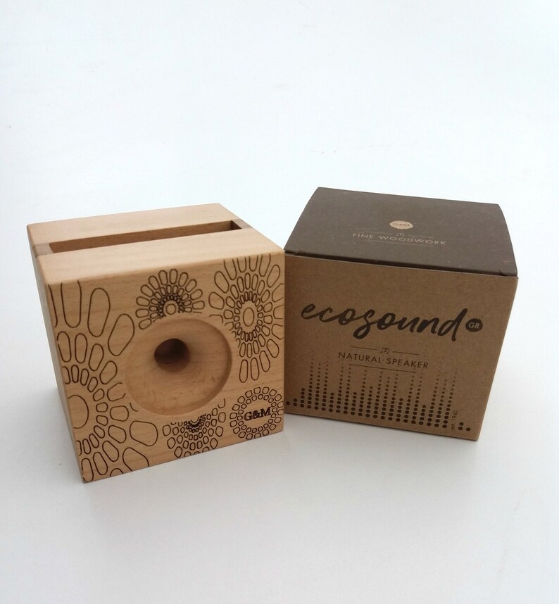 May include: A wooden speaker with a circular cutout and a geometric pattern. The speaker is packaged in a brown box with the text "ecosound" and "natural speaker".