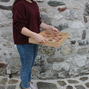 K&ouml;nnte beinhalten: Ein Serviertablett aus Holz mit einem einzigartigen Design aus kleinen Holzst&uuml;cken. Das Tablett hat zwei Griffe an den Seiten und wird von einer Person gehalten.