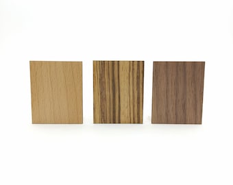 May include: Three rectangular wood samples. The first is a light tan color, the second has a zebra wood pattern with dark brown and tan stripes, and the third is a dark brown color. All three are displayed against a white background.