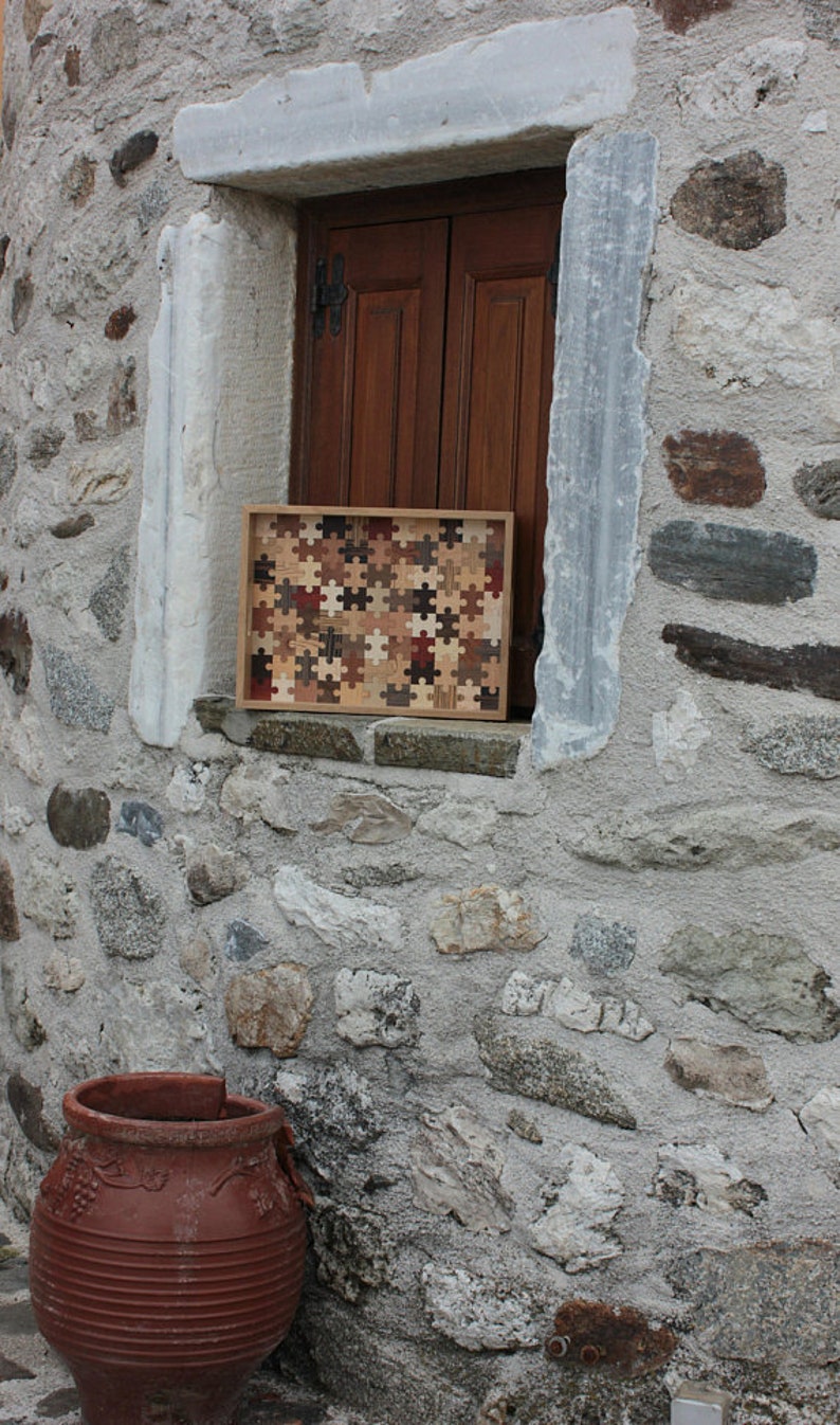 K&ouml;nnte beinhalten: Ein Tablett aus Holz, das aus kleinen Puzzleteilen in verschiedenen Braunt&ouml;nen, Beige und Rot besteht. Das Tablett liegt auf einer Steinmauer mit einem Fenster dahinter.