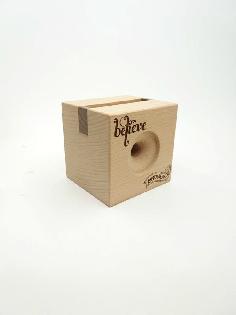 May include: A wooden phone stand with a cutout for a phone and the words "believe in your dream" engraved on the front.