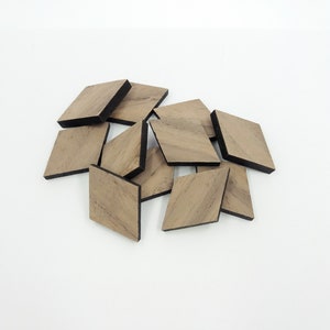 Op de afbeelding: Een stapel kleine, houten ruitvormige vormen met zwarte randen. De ruiten zijn in een willekeurig patroon gerangschikt.