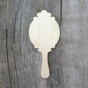 May include: A wooden cutout of a hand mirror with a decorative frame and handle. The mirror is blank and ready to be painted or decorated.