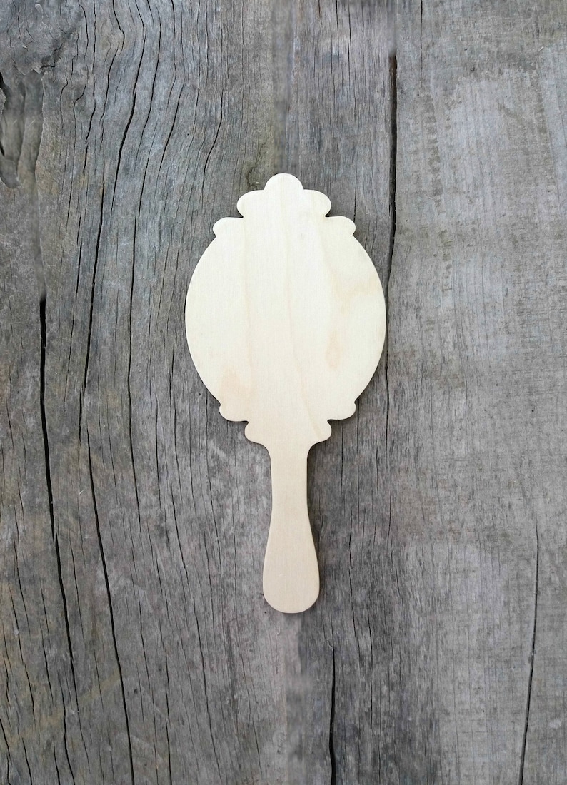 May include: A wooden cutout of a hand mirror with a decorative frame and handle. The mirror is blank and ready to be painted or decorated.