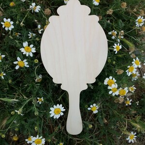 May include: A wooden hand mirror with a decorative, ornate frame. The mirror is blank and ready to be painted or decorated.