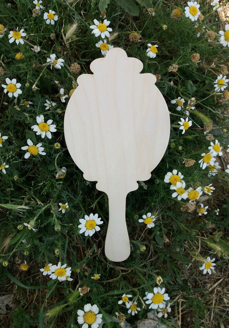May include: A wooden hand mirror with a decorative, ornate frame. The mirror is blank and ready to be painted or decorated.