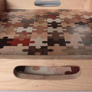 K&ouml;nnte beinhalten: Ein Tablett aus Holz mit einem Puzzle-Design aus verschiedenen Holzarten. Das Tablett hat zwei Griffe an den Seiten.