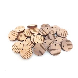 May include: A pile of small, circular wooden pendants. Each pendant has a hole for threading and is decorated with etched parallel lines. The pendants are a light brown colour and appear to be made of natural wood.