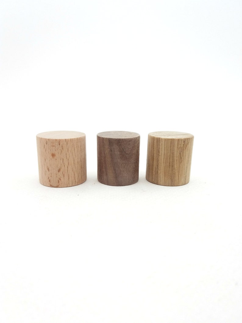 Peut inclure: Trois cylindres en bois de diff&eacute;rents types de bois. Le cylindre de gauche est brun clair, le cylindre du milieu est brun fonc&eacute; et le cylindre de droite est brun clair avec un motif de grain.