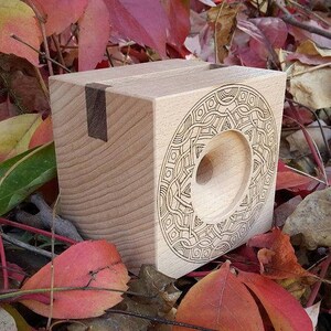 May include: A wooden box with a circular cutout and an intricate geometric design carved into the front. The box is made of light wood with a dark wood inlay.
