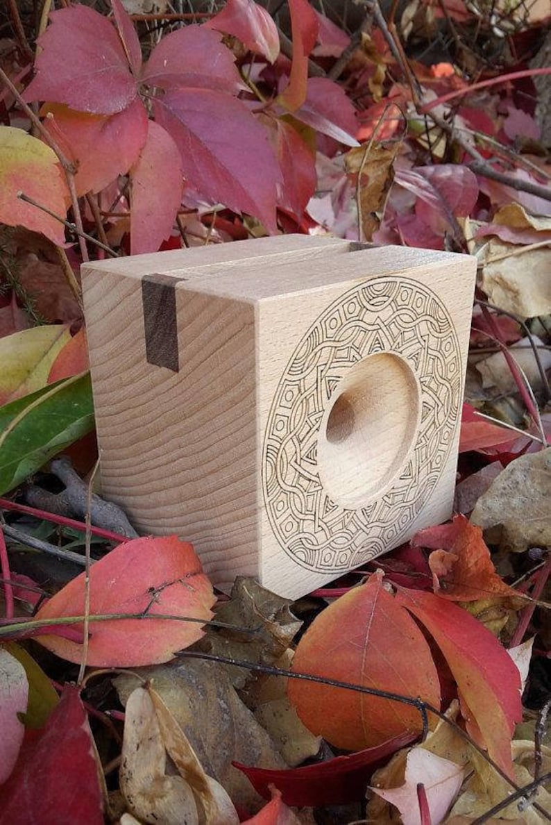 May include: A wooden box with a circular cutout and an intricate geometric design carved into the front. The box is made of light wood with a dark wood inlay.