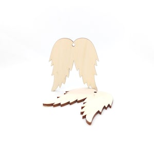 May include: Two wooden angel wing ornaments. The wings are light brown with a darker brown edge and a small hole at the top for hanging. The wings are displayed on a white background.