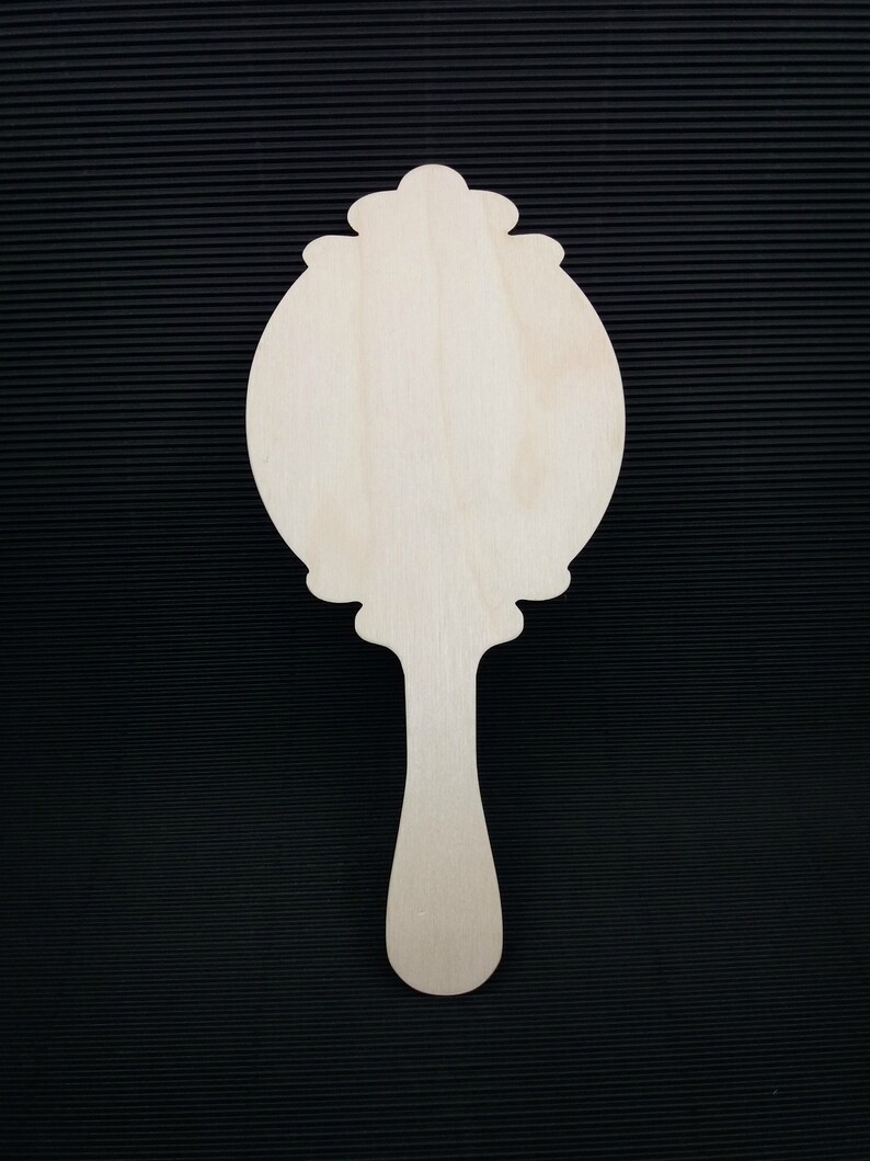 May include: A wooden hand mirror with a decorative, ornate frame and a long handle. The mirror is blank and ready to be painted or decorated.