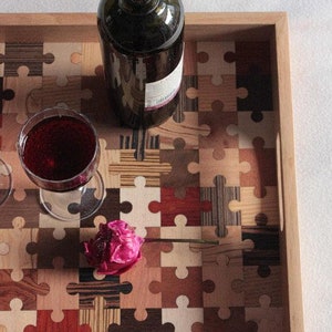 K&ouml;nnte beinhalten: Ein Holztablett mit einem Puzzle-Design aus verschiedenen Holzst&uuml;cken in verschiedenen Farben. Auf dem Tablett stehen eine Flasche Rotwein und ein Glas Rotwein sowie eine rosa Blume.