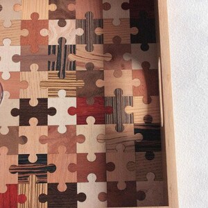 K&ouml;nnte beinhalten: Ein Tablett aus Holz mit einem Puzzle-Design aus verschiedenen Holzarten. Das Tablett hat einen Griff an der Seite.