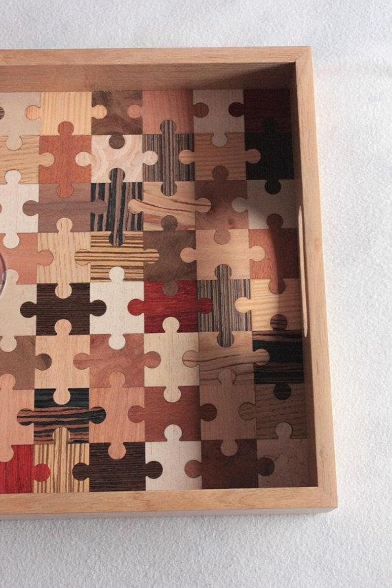 K&ouml;nnte beinhalten: Ein Tablett aus Holz mit einem Puzzle-Design aus verschiedenen Holzarten. Das Tablett hat einen Griff an der Seite.