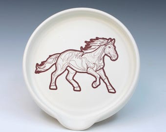 May include: White ceramic spoon rest with a brown outline of a running horse. The spoon rest has a curved shape with a small indentation for resting utensils. The horse design is centered on the rest.