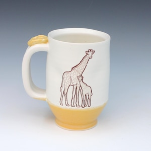 May include: White ceramic mug with a yellow base and handle, featuring a brown giraffe illustration. The handle has a decorative yellow accent. The mug is designed for hot beverages.
