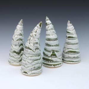 May include: Four conical ceramic sculptures with a white glaze and horizontal ridges. Each piece features a distinct green drip pattern that follows the textured grooves, creating a layered effect across the surface of the tapered, spiraling forms.