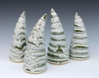 May include: Four conical ceramic sculptures with a white glaze and horizontal ridges. Each piece features a distinct green drip pattern that follows the textured grooves, creating a layered effect across the surface of the tapered, spiraling forms.