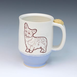 May include: A ceramic mug with a light blue base and a white upper section. A brown outline of a corgi dog is on the white section. The handle has a small, yellow, decorative element. The mug is approximately 4 inches tall.