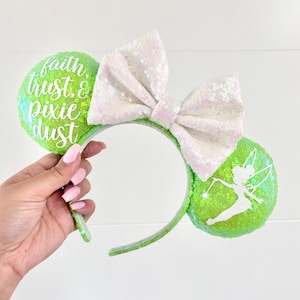 May include: Green and white Minnie Mouse ears with a white bow and the text "faith, trust, & pixie dust" on one ear and a silhouette of Tinkerbell on the other ear.