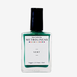 May include: A clear glass nail polish bottle with a black cap. The bottle contains green nail polish and has a white label with the word "VERT" and the text "New York City METROLINEAS". The bottle contains 15ml of polish.