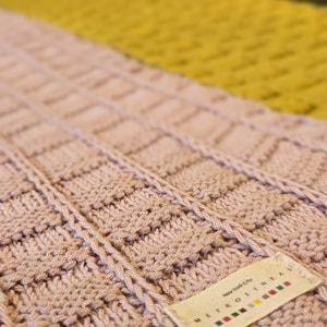 Pu&ograve; includere: Un primo piano di una sciarpa di maglia rosa con un'etichetta bianca che recita "New York City METRO LINEN". L'etichetta presenta un design a righe colorate.