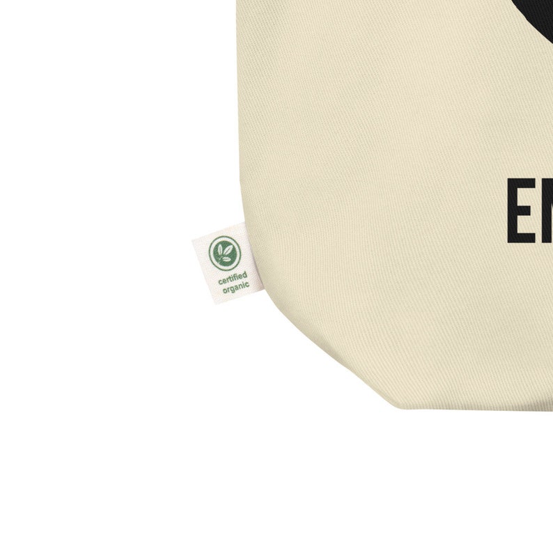 May include: A beige tote bag with a black graphic and the text "Enjoy" printed on the front. The bag has a green certified organic label.