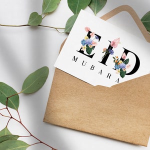 May include: A white card with the words "Eid Mubarak" written in black lettering. The letters are decorated with colorful flowers. The card is in a brown envelope.