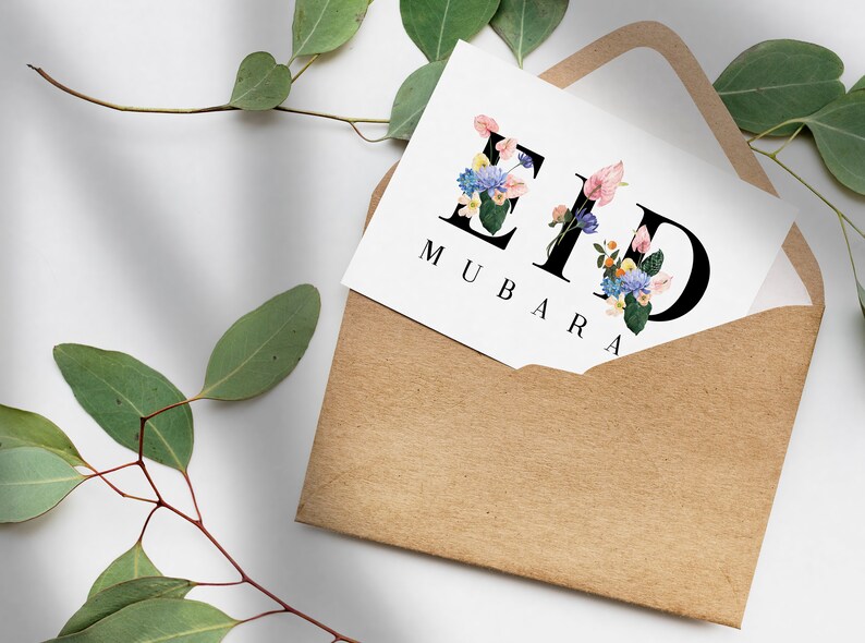 May include: A white card with the words "Eid Mubarak" written in black lettering. The letters are decorated with colorful flowers. The card is in a brown envelope.