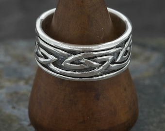 May include: A silver ring with a Celtic knot design. The ring is on a wooden ring holder.