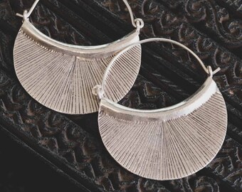 May include: A pair of silver hoop earrings with a fan-shaped design. The earrings are made of metal and have a shiny finish.