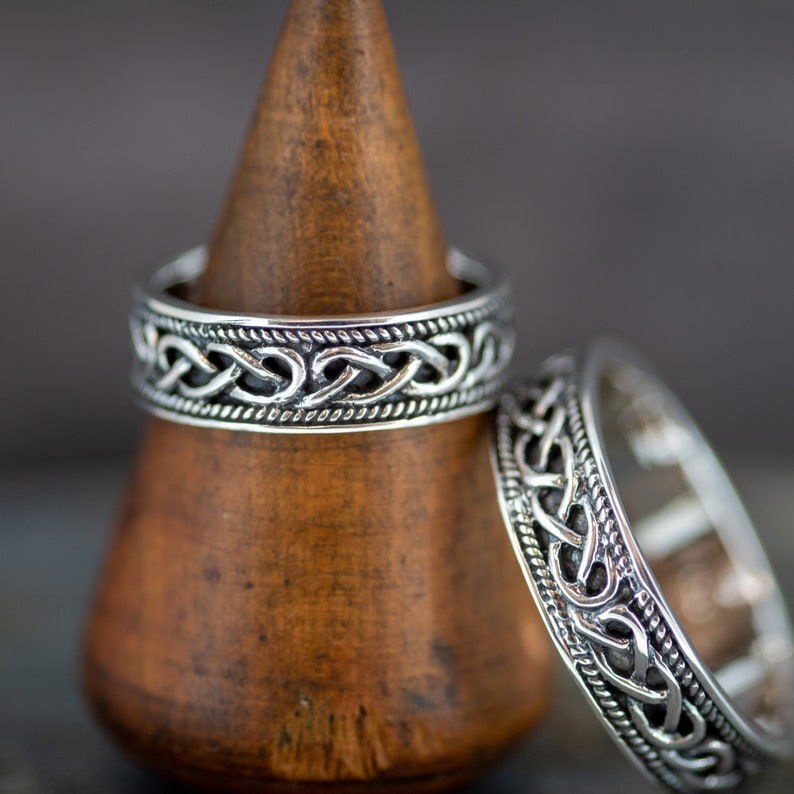 May include: Two silver rings with a Celtic knot design. The rings are displayed on a wooden ring holder.