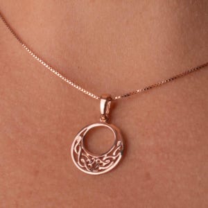 Op de afbeelding: Een ketting met een ros&eacute;gouden hanger. De ronde hanger heeft een ingewikkeld Keltisch knoopontwerp. De fijne ketting ondersteunt de hanger. De ketting wordt getoond tegen een neutrale achtergrond.