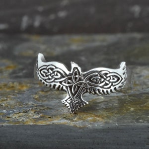 May include: A silver ring with a Celtic knot design in the shape of a bird. The ring is detailed and intricate.