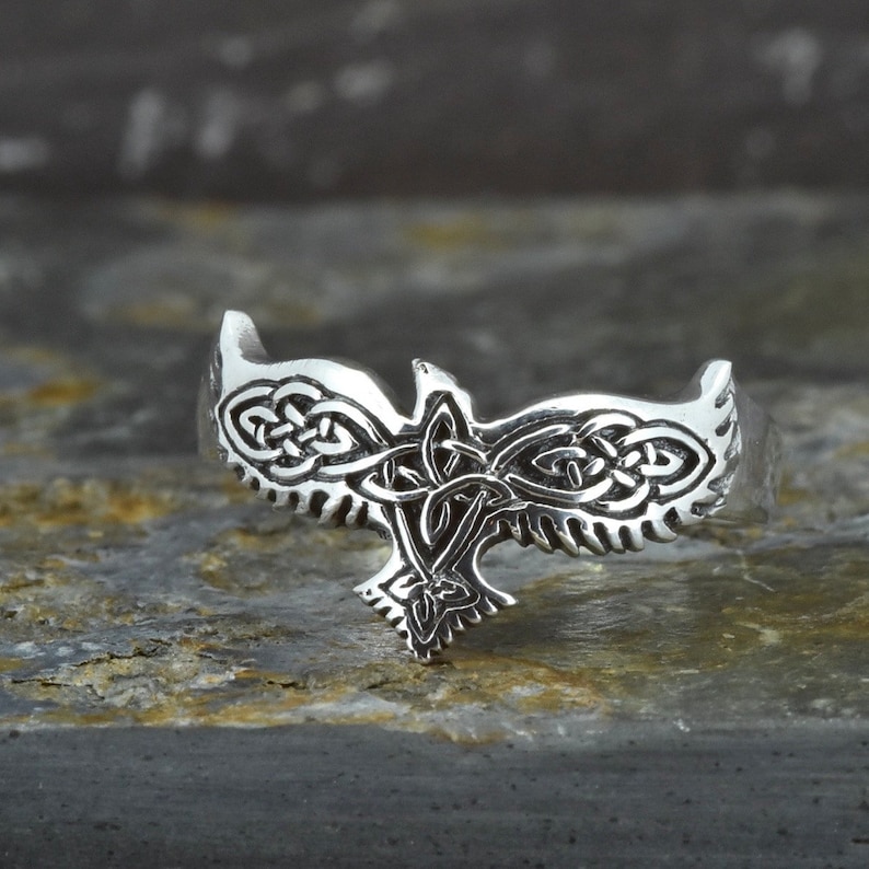 May include: A silver ring with a Celtic knot design in the shape of a bird. The ring is detailed and intricate.