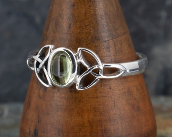 Può includere: Un anello d'argento con una pietra preziosa verde incastonata in un design a nodo celtico.