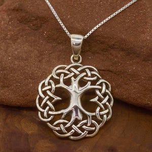 Puede incluir: Un collar de plata con un colgante de árbol de la vida con nudo celta. El colgante es de diseño circular con un árbol en el centro y un intrincado trabajo de nudos a su alrededor.