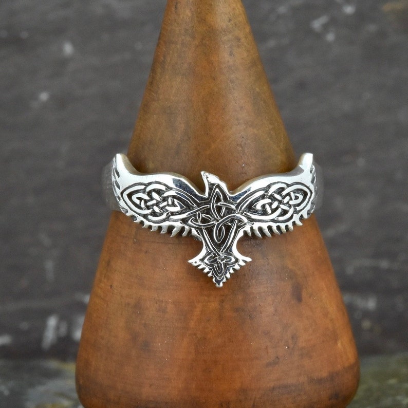 May include: A silver ring with a Celtic knot design featuring a stylized eagle. The eagle's wings are spread and the knotwork is intricate.