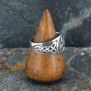 May include: A silver ring with a Celtic knot design. The ring is on a wooden display stand.